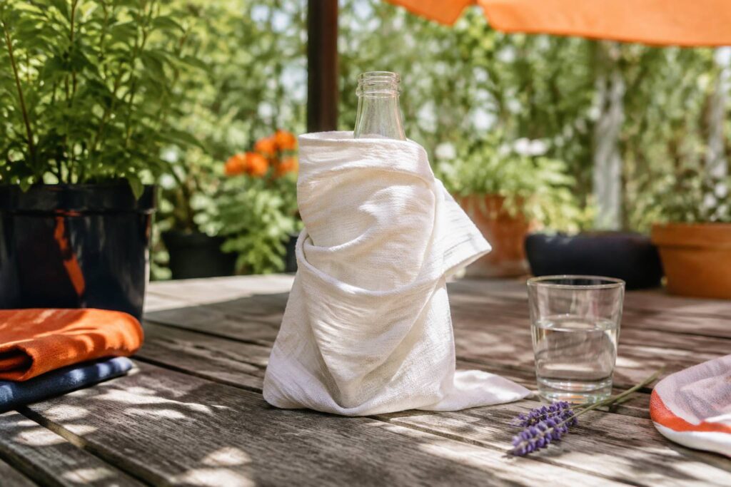 Bouteille d'eau enveloppée d'un torchon humide posée à l'ombre sur une table de jardin